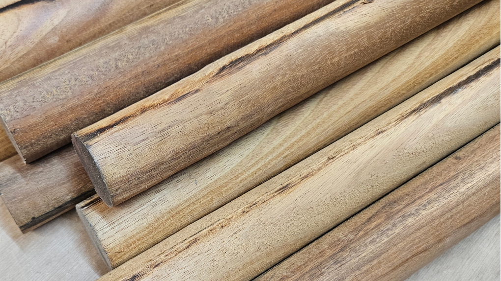 Close-up van meerdere ronde, massieve hardhouten staven met een natuurlijke bruine nerf, klaar voor verwerking als armleuningen.