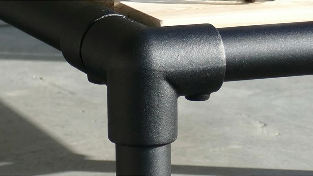 Close-up van een T-vormig zwart koppelstuk van een industrieel buisframe met een zwarte poedercoating afwerking.