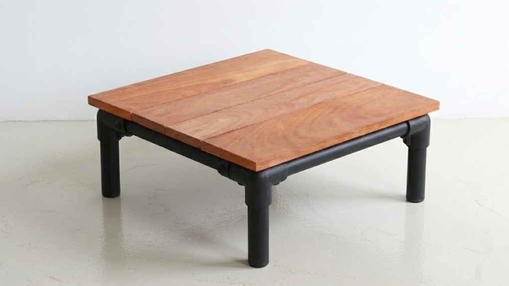 Een industriële loungetafel met een tafelblad van vier brede, roodbruine hardhouten planken op een zwart metalen buisframe.