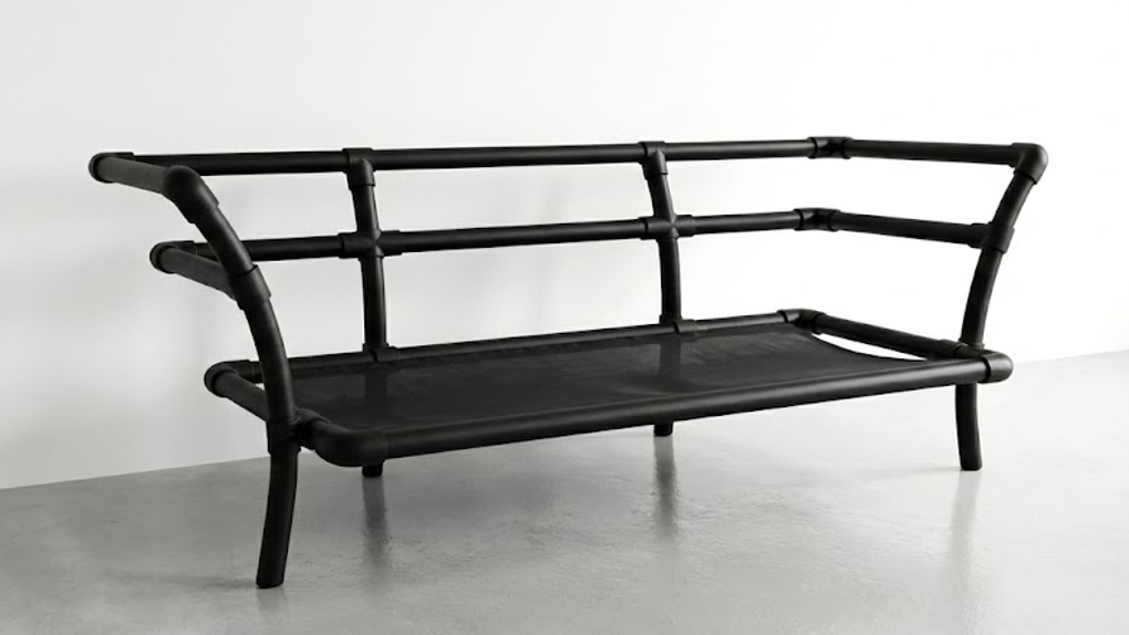 Een close-up van het zwarte industriële buisframe van een bank waarin een strakgespannen zwart gaas-materiaal is gemonteerd als basis voor de kussens.